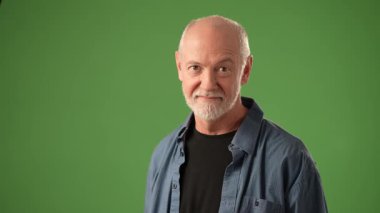 Olgun bir adam duygularını ifade etmek için el hareketlerini kullanırken baş parmağını kaldırır ve gülümser. Fotoğrafta ifadesini vurgulayan koyu yeşil bir arkaplan var..