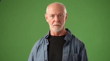 Olgun bir adam, yeşil bir zeminde parmaklarını kulaklarına bastırarak çeşitli duygular gösterir. İfadesi şu anda yoğunluğu ve dramı ifade ediyor..