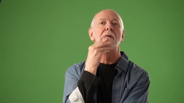 Üst düzey bir adam, yeşil ekran arkaplanına kurulmuş güzel anılarla düşünceli bir şekilde poz verir, ifadesini vurgulayan bir portre ortamında çeşitli duygular sergiler..