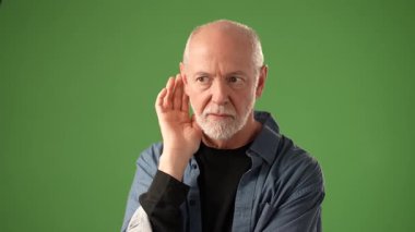 Olgun bir adam, düşünceli bir ifadeyle ve bir sırrı saklama önerisiyle, katı yeşil bir ekran arkaplanına karşı, portre oturumu sırasında bir anlık tefekkür ve duygu sergiliyor..