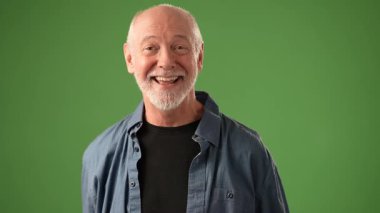 Sakallı olgun bir adam, neşeli hareketlerle gülümserken duygularını belli eder. Ayarlar, onun ifadesel duruşunu geliştiren katı yeşil ekran arkaplanı içeriyor..