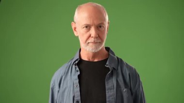 Neşeli bir gülümsemesi olan olgun bir adam ellerini katı yeşil bir ekranın önünde çırpıyor. Duyguları bir kutlama anında mutluluk ve bağlılık iletir..