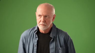 Olgun bir adam, güçlü bir duyguyu ifade eden, katı yeşil bir arka plana karşı poz verir. Düşünceli bakışları ve ciddi tavırları derinlik ve gücü çağrıştırıyor..