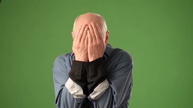 Beyaz saçlı ve sakallı olgun bir adam kutlama için sevinçle yumruklarını kaldırır. Sert yeşil perde arkasında güçlü duygular gösterir..