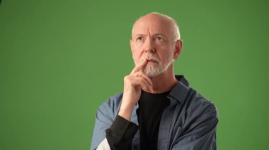 Olgun bir adam neşeli bir ifadeyle, canlı yeşil bir ekran karşısında seyirciyi işaret eder. Davranışları, bağlılık ve güven öneriyor..