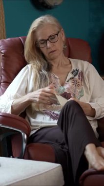 Gülümseyen, olgun bir kadın rahat bir sandalyeye oturur, bir mektup okurken gözleri sevinçle doludur. Uzun saçları özgürce akıyor ve rahatlatıcı bir kıyafet giyiyor..