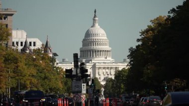 Washington DC 'de Capitol Binası' nın arka planında bir sokak sahnesi. Trafik kırmızı ışıkta durdu ve yayalar caddeyi geçti. Birkaç tabela, ağaç ve sokak lambası.