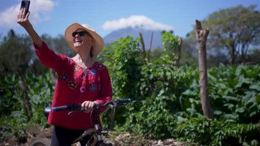 Gülümseyen son sınıf öğrencisi bir kadın Ometepe Adası 'nda bisiklet sürmekten hoşlanıyor. Güneşli bir günde, Volkan Concepcion' un arka planında telefonuyla fotoğraf çekiyor..