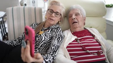 90 'lı yaşlarda yaşlı bir kadın kızıyla görüntülü konuşma yapmaktan hoşlanıyor. Kanepede rahatça oturup telefonda gülüşlerini ve hikayelerini paylaşıyorlar..