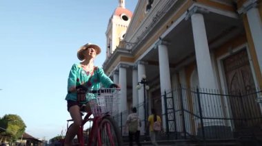 Gülümseyen olgun bir kadın Nikaragua, Granada 'daki çarpıcı katedralin önünde bisikletini mutlulukla sürüyor. Açık gökyüzü onun açık hava macerasına neşe katıyor..