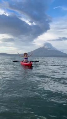 Günbatımında Nikaragua Gölü 'nün sakin sularında kano süren mutlu bir kadının dikey videosu. Arka planda Orta Amerika' daki Ometepe Adası 'ndaki görkemli Gebelik Yanardağı var..