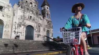 Gülümseyen bir kadın bisikletiyle Granada, Nikaragua 'daki Iglesia Guadalupe' nin dışında güneşli bir günde Orta Amerika 'nın canlı atmosferini yaşıyor..