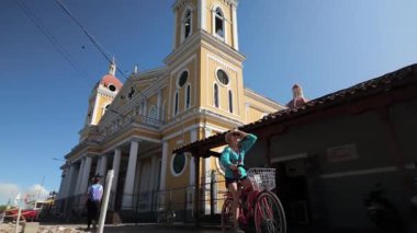 Granada, Nikaragua - 01: 20 2025: Olgun bir kadın, arka planda çarpıcı bir katedrali olan Granada, Nikaragua 'da bisiklet sürmekten hoşlanıyor. Sıcak güneş ve renkli mimari onun açık hava macerasını geliştirir..
