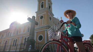 Olgun bir kadın bisikletiyle Granada, Nikaragua 'yı keşfediyor. Renkli katedrale ve Orta Amerika' nın canlı atmosferine hayranlıkla gülüyor..