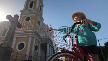Olgun bir kadın Granada, Nikaragua 'da bisiklet sürmekten hoşlanıyor, katedral yakınındaki canlı mimariyi ve ılık güneşi alıyor ve yemyeşil yemyeşil..
