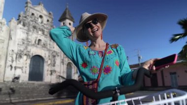 Granada, Nikaragua 'daki güzel Iglesia Guadalupe kilisesinin yanında bisiklet sürerken gülümseyen mutlu bir turistin portresi. Parlak atmosfer onun neşeli seyahat deneyimini yansıtıyor..