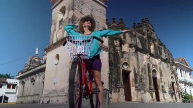 Olgun bir kadın bisikletiyle Granada, Nikaragua 'daki tarihi La Merced kilisesinin önünde keyif içinde poz veriyor, Orta Amerika' daki açık hava deneyimini kucaklıyor..