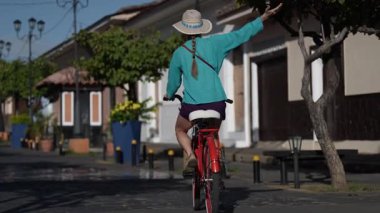 Olgun bir kadın bisikletini Granada, Nikaragua 'nın büyüleyici sokaklarında sürüyor. Açık hava macerası ve yerel kültürün tadını çıkarırken gülümsüyor..