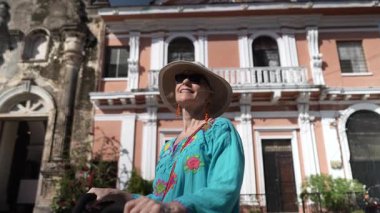 Parlak kıyafetli mutlu bir turist, Nikaragua, Granada 'daki La Merced Kilisesi' nin dışında bisiklet sürerken ve canlı şehir atmosferini keşfederken başparmak kaldırıyor..