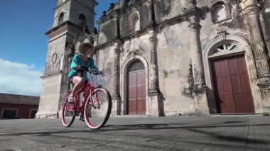 Olgun bir kadın bisikletini Granada, Nikaragua 'daki tarihi La Merced Kilisesi' nin önünde gülerek sürüyor, canlı bir kültüre ve ılık havaya boğuluyor..