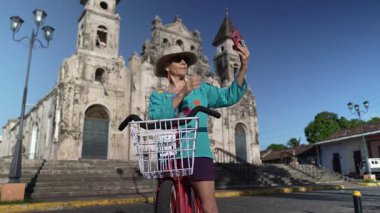 Olgun bir kadın Nikaragua, Granada 'da Iglesia de Guadalupe dışında bisiklet sürmekten zevk alır. Yerel kültüre dalmışken telefonuyla selfie çekiyor..