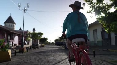 Olgun bir kadın, güneşli bir günde Orta Amerika 'nın cazibesini tecrübe ederek La Merced, Granada, Nikaragua' nın pitoresk Calzada caddelerinde bisiklet sürmekten hoşlanır..
