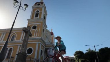 Gülümseyen mutlu bir turist Granada, Nikaragua 'da bisiklet deneyiminin keyfini çıkarıyor. Arka planda açık gökyüzünün altında güzel bir katedral var..