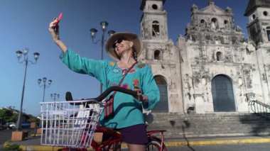 Olgun bir kadın bisikletiyle Iglesia Guadalupe 'nin dışında selfie çekiyor, Granada, Nikaragua' nın güzelliğini yakalıyor, canlı turist atmosferini deneyimlerken..
