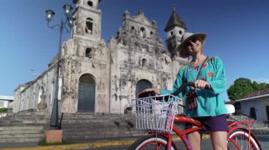 Olgun bir kadın, Granada, Nikaragua 'daki tarihi Iglesia de Guadalupe' nin önünde bisiklet sürerken gülümseyerek başparmağını kaldırıyor ve Orta Amerika macerasının tadını çıkarıyor..