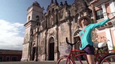 Olgun bir kadın bisikletiyle La Merced Kilisesi 'nin önünde dururken gülümsüyor. Güneşli günün ve Granada, Nikaragua 'nın canlı atmosferinin tadını çıkarıyor..