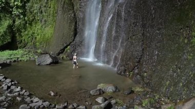 Olgun bir kadın, Nikaragua, Ometepe Adası 'ndaki San Ramon şelalesinin ferahlatıcı sularında yürüyor. Etrafı yemyeşil ormanlarla çevrili ve Orta Amerika' da canlı bir gökkuşağı var..