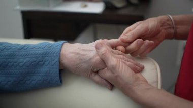 Bakıcı, yaşlı bir kadının elini nazikçe tutar, bir sağlık merkezinde bağ ve desteği destekler, duygusal bağlılığı ve bakımı teşvik eder..