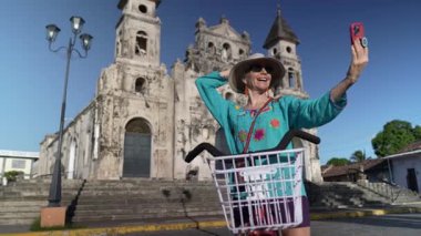 Mutlu bir kadın, Granada, Nikaragua 'da bisiklete binmekten keyif alırken, tarihi Iglesia Guadalupe Kilisesi' nin önünde açık bir gökyüzünün altında telefonuyla selfie çekiyor..