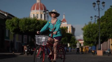 Gülümseyen olgun bir kadın bisikletiyle Granada, Nikaragua 'dan geçiyor, büyüleyici atmosferi ve zengin kültürü yaşıyor. Bu açık hava macerasında güneş parlıyor..