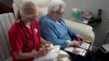 Önlüklü bir bakıcı ilaç detaylarını kaydeder. Yaşlı bir kadın ise oturma odasında fotoğraf albümlerine bakar. Arkadaşlık ve ilgi gösterir..