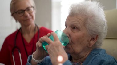 Bakıcı, sıcak bir öğleden sonra sıcacık bir sağlık merkezinde mavi bardaktan su içmesine yardım eden yaşlı bir kadınla yakınlaşıyor..