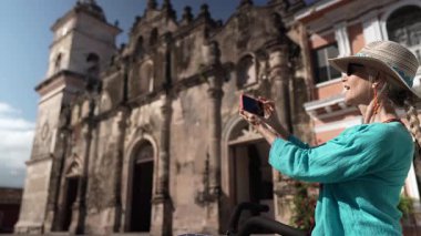 Mutlu bir turist telefonuyla Granada, Nikaragua 'daki La Merced Kilisesi' nin önünde fotoğraf çekiyor. Bisiklete biniyor ve açık hava deneyiminin tadını çıkarıyor..