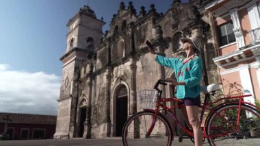 Mutlu bir turist telefonu ile Granada, Nikaragua 'daki La Merced Kilisesi' nin önünde selfie çeker. Bisiklete biniyor ve açık hava deneyiminin tadını çıkarıyor..