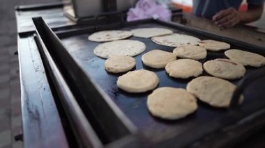 Bir sokak satıcısı Granada, Nikaragua 'da sıcak bir ızgarada taze pupusas ve quesillo pişiriyor. Yerel halk ve turistler canlı pazar atmosferinin keyfini çıkarırken geleneksel yiyeceklerin tadını çıkarıyorlar..