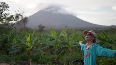 Güzel, son sınıf öğrencisi bir kadın Omotepe Adası 'nda yemyeşil bir araziyle çevrili bisiklet sürüyor. Concepcion volkanı arka planda görkemli bir şekilde beliriyor.