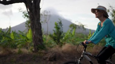 Gülümseyen olgun bir kadın Ometepe Adası 'nda verimli bir çevrede bisiklet sürmekten zevk alırken arka planda muhteşem Concepcion volkanı Orta Amerika' da doğal güzellikleri gözler önüne seriyor..
