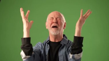 Gri sakallı olgun bir adam yoğun duygular gösterir, heyecanla ya da kutlamayla yumruklarını kaldırır. Som yeşil bir zemine karşı duruyor..