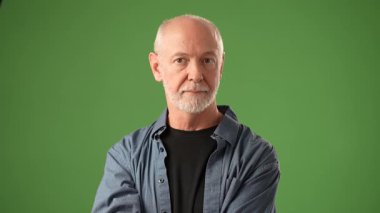Dostane bir gülümsemesi olan kıdemli bir adam yeşil bir ekrana karşı duruyor, sıcaklığı ve güveni var. Sıradan bir kıyafet giyiyor, rahat bir tavır sergiliyor..
