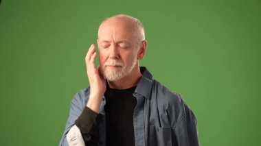 Gri saçlı ve sakallı olgun bir adam canlı yeşil bir arkaplan karşısında kaslarını gösteriyor ve etkileyici bir enerji anı yakalıyor..