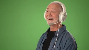 Kulaklık takan olgun bir adam, saf yeşil bir arka plana karşı duruyor. Ürün duyurusuna özgüvenle hazırlanırken duygularını ifade ediyor..