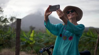 Renkli bluzlu mutlu bir son sınıf güzeli, Ometepe Adası 'nın arka planında yemyeşil bir yeşil ile çevrili Concepcion volkanı ile neşeli bir selfie çeker..