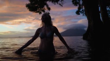 Neşeli, olgun bir kadın gün batımında sakin bir gölün sularında yürür. Concepcion volkanı arka planda görünür. Huzurlu bir atmosfer yaratır..
