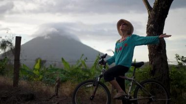 Gülümseyen kadın Nikaragua 'daki görkemli Concepcion volkanı tarafından çerçevelenen Ometepe Adası' nda bisiklet sürerken kollarını kaldırarak canlı doğal manzarayı kucaklıyor..