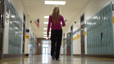 Berkeley Springs, WV, ABD - 125 2024: Mor kazaklı olgun bir kadın okul koridorunda dolaplarıyla yürüyor. Sahne onu bir sonraki dersine giderken yakalıyor, odaklanmış ve kendini işine adamış..