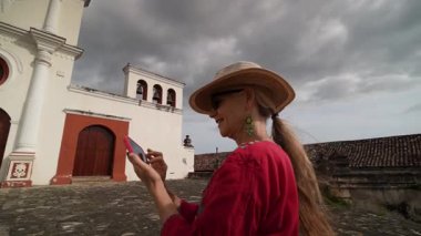 Olgun bir kadın, Granada, Nikaragua 'daki bir manastıra yaptığı ziyaretten zevk alıyor, akıllı telefonuyla dramatik bir gökyüzüne karşı yaşadığı deneyimi yakalıyor..